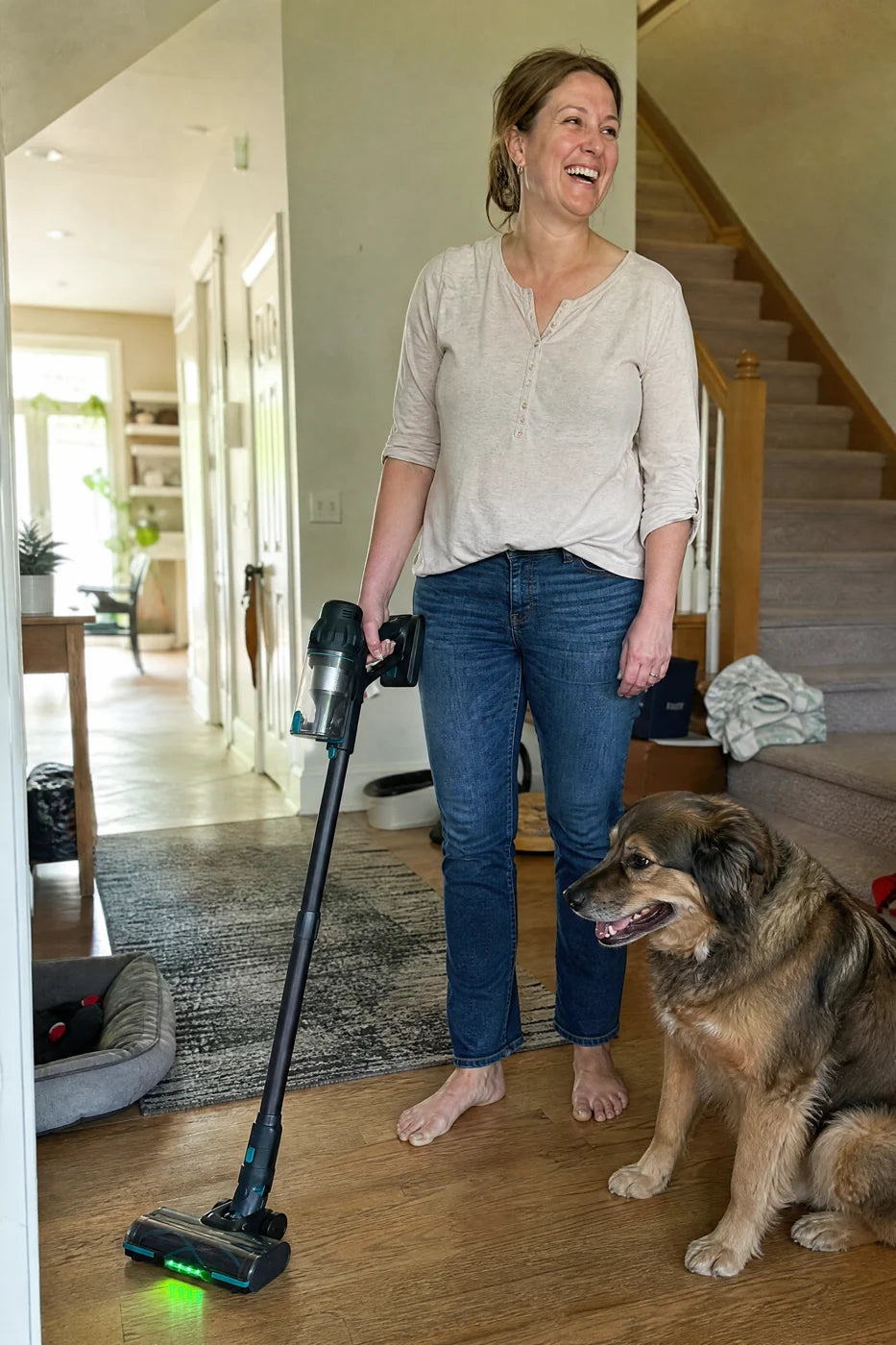 A woman holding Puravo Stick in one hand in a bright hallway with her dog beside her