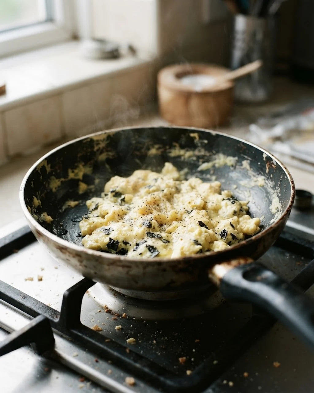 Scrambled eggs in a worn pan with black flakes of coating mixed through them